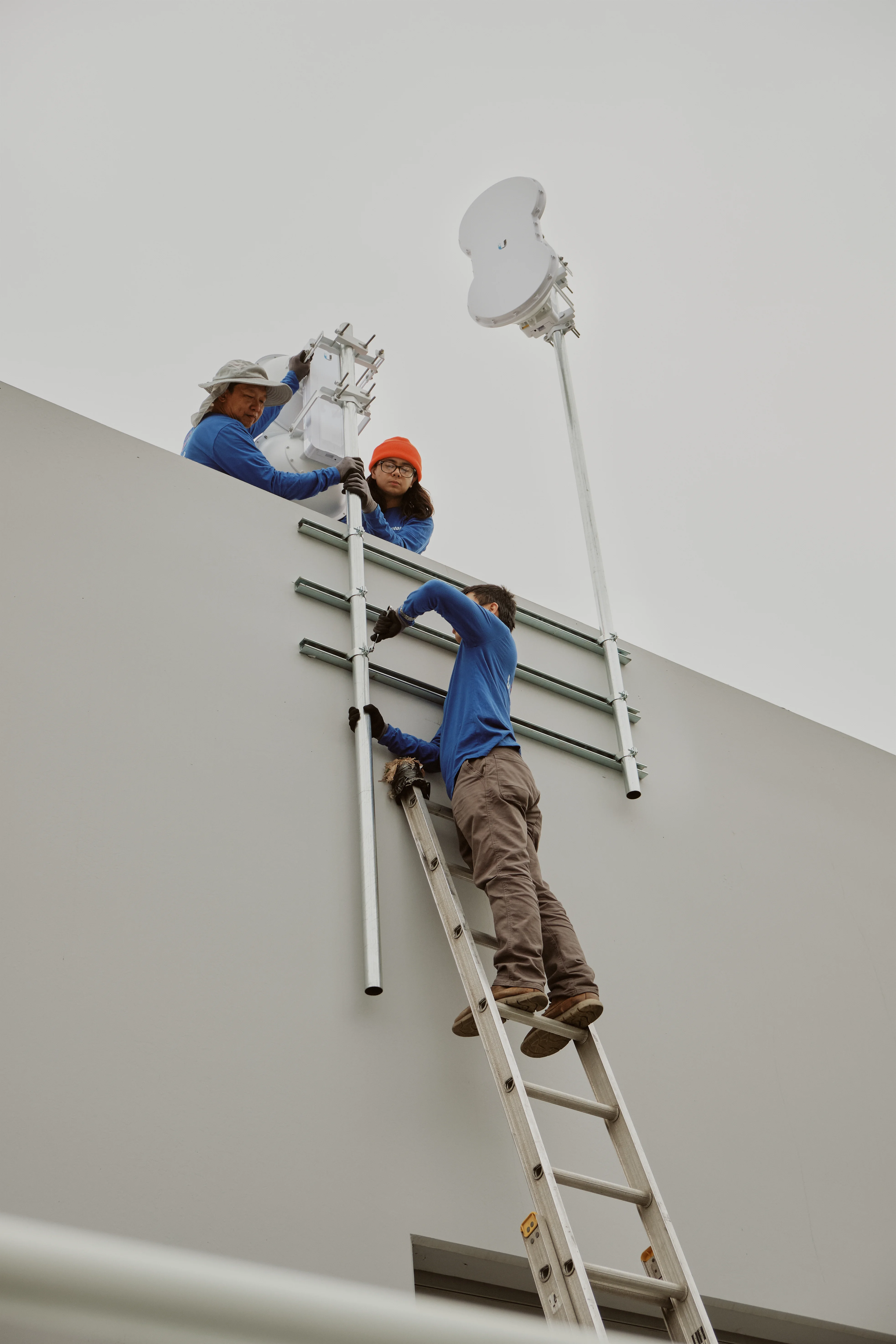 Technicians running conduit and mounting struts up a rooftop parapet for a point-to-point wireless bridge