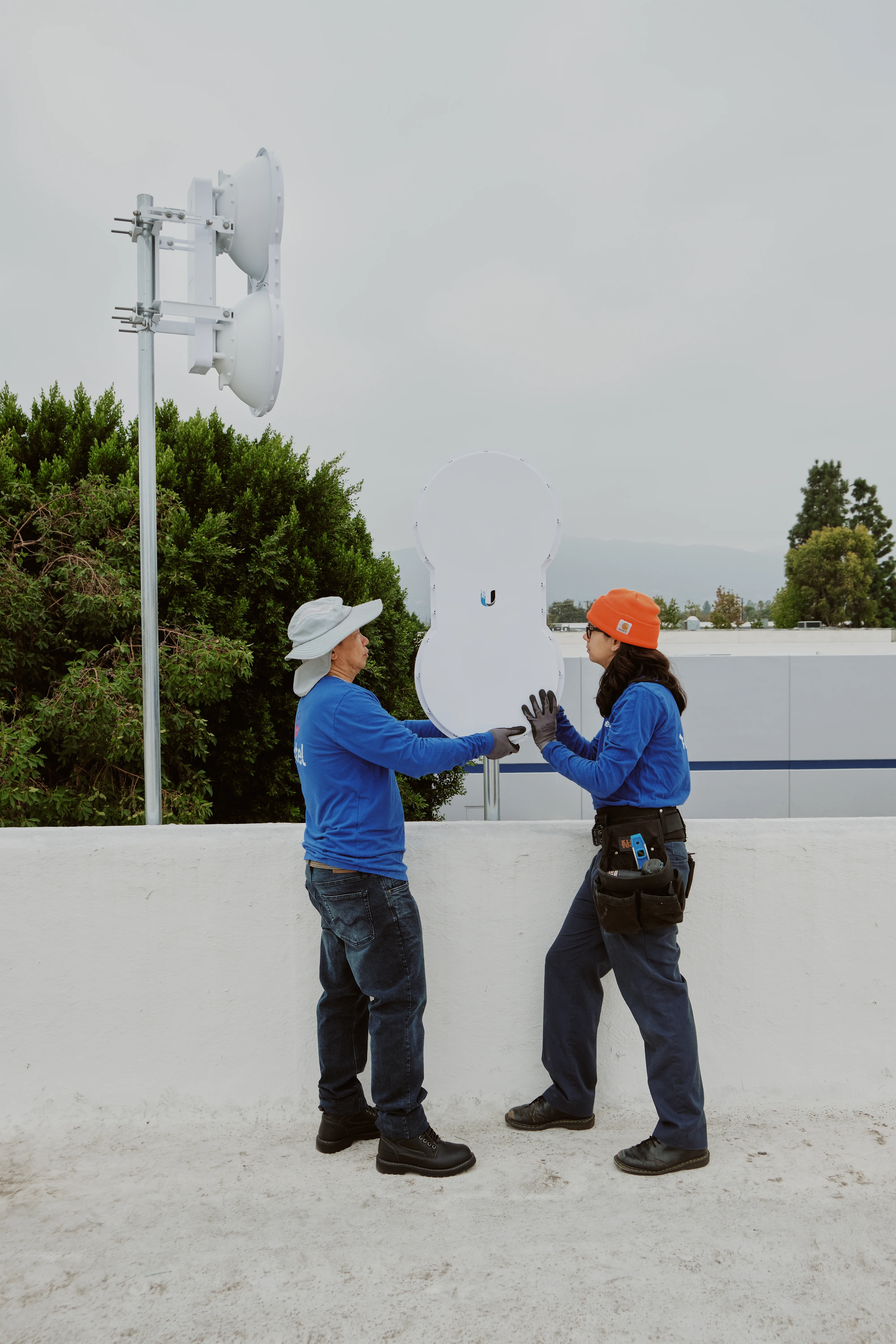 AllTime Systems technicians handling a Ubiquiti airFiber AF-5U dish before mounting it on the rooftop mast