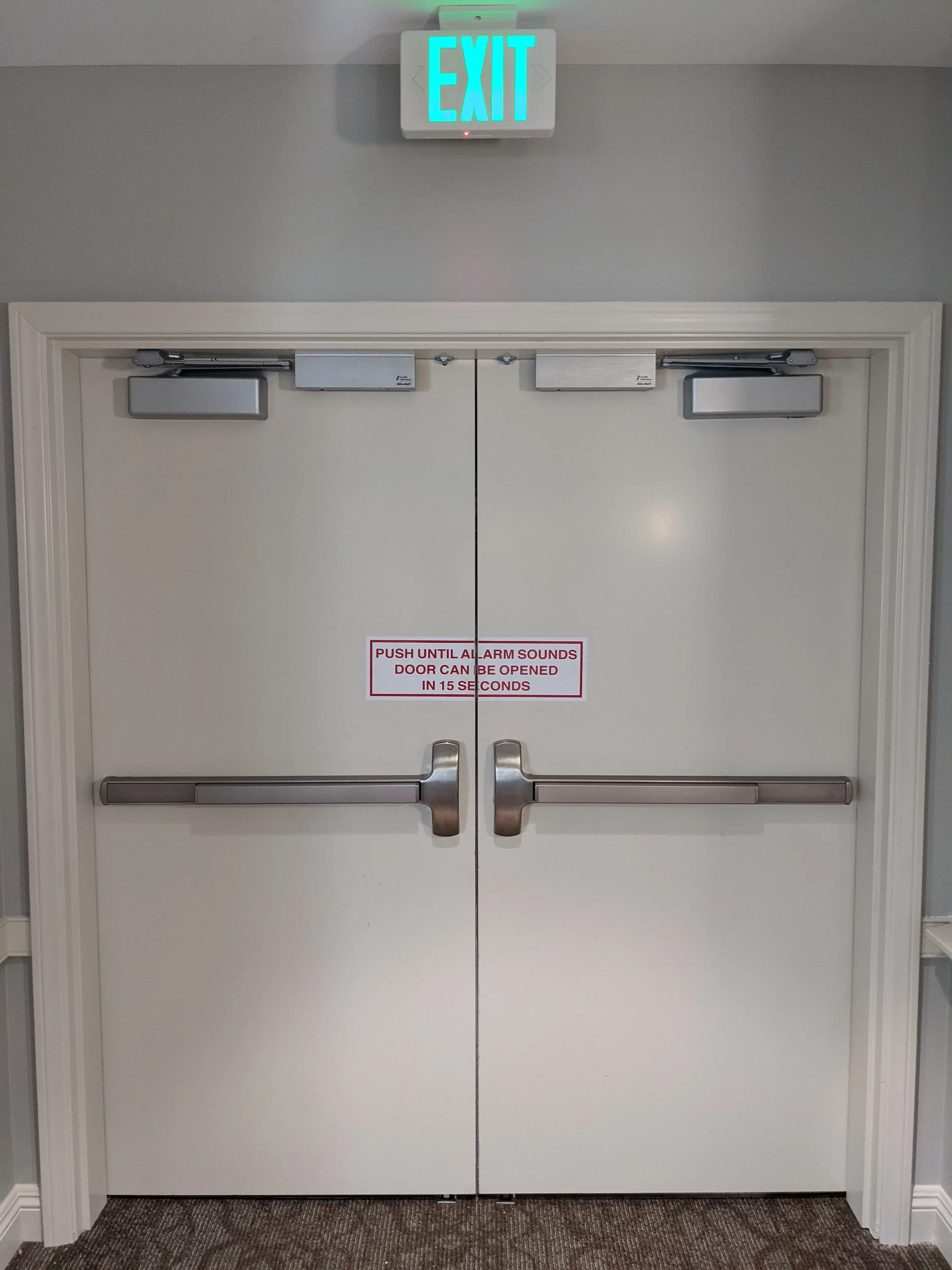 Delayed egress exit doors with panic bar hardware and alarm delay signage at a memory care senior living facility