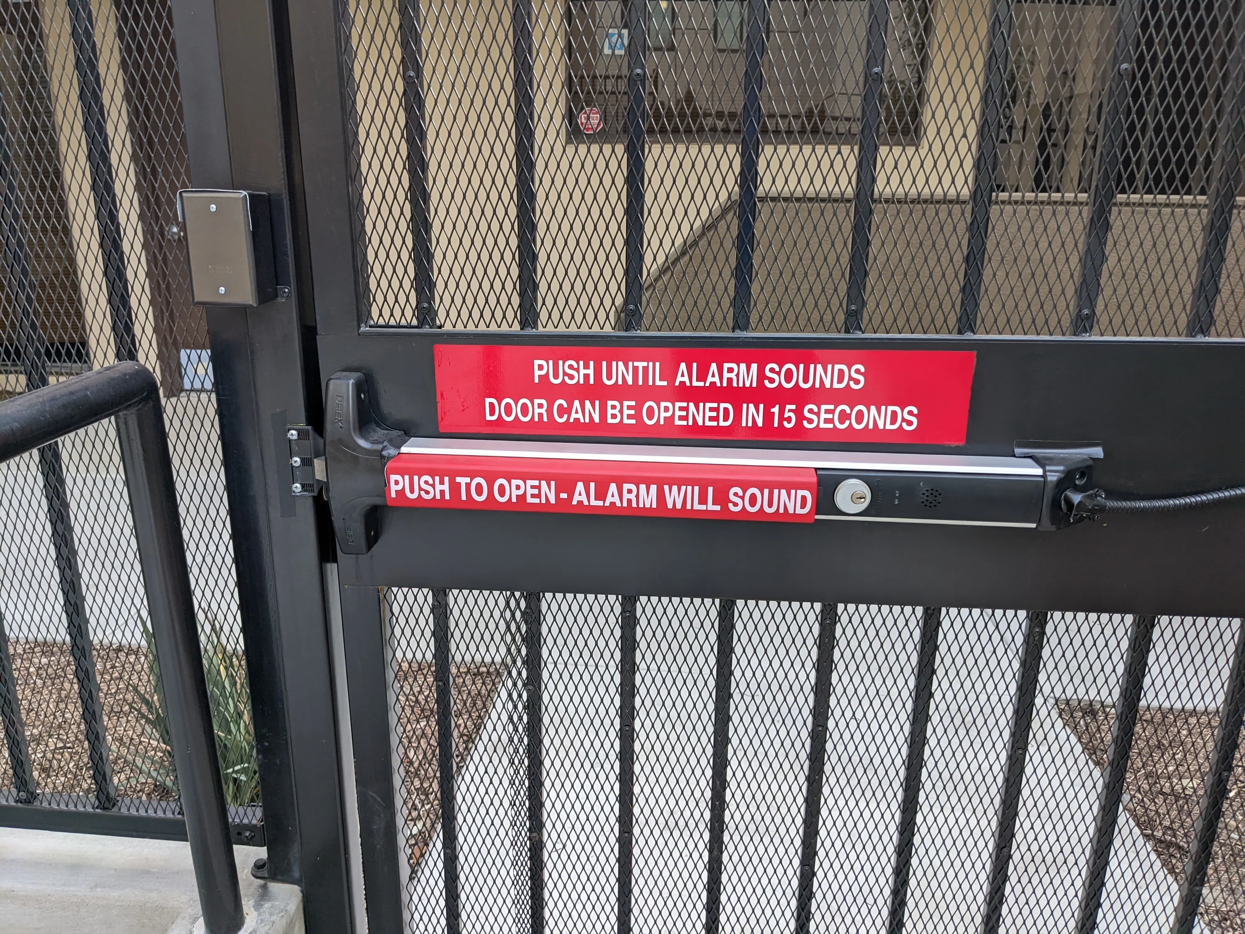 Exterior gate with delayed egress panic hardware reading push to open, alarm will sound, door can be opened in 15 seconds